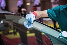 A man in a green shirt and blue gloves cleaning a car windshield.


