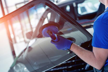 A man in a blue shirt holding a cleaning cloth, cleaning a car window with focused determination.


