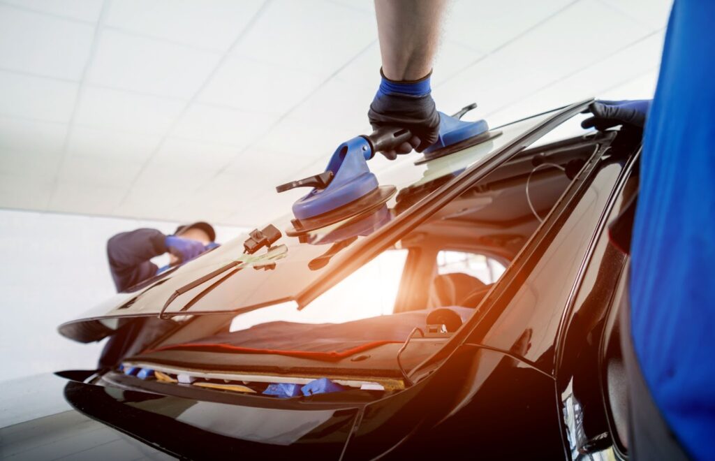 A man wearing a blue glove is repairing a cars auto glass specifically the cracked windshield.