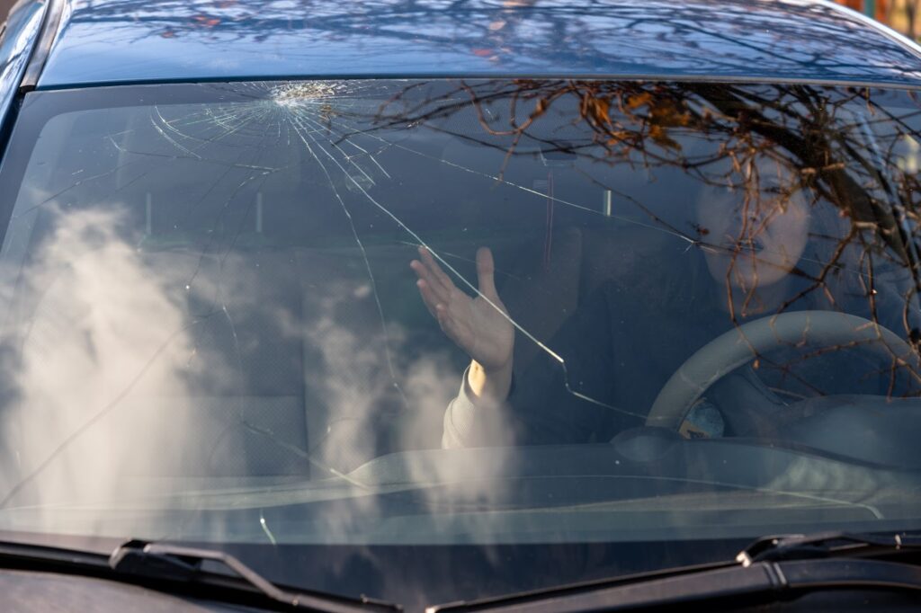 A woman sits in the drivers seat of a car, with cracked windshield undergoing auto glass replacement for vehicle glass repairs.