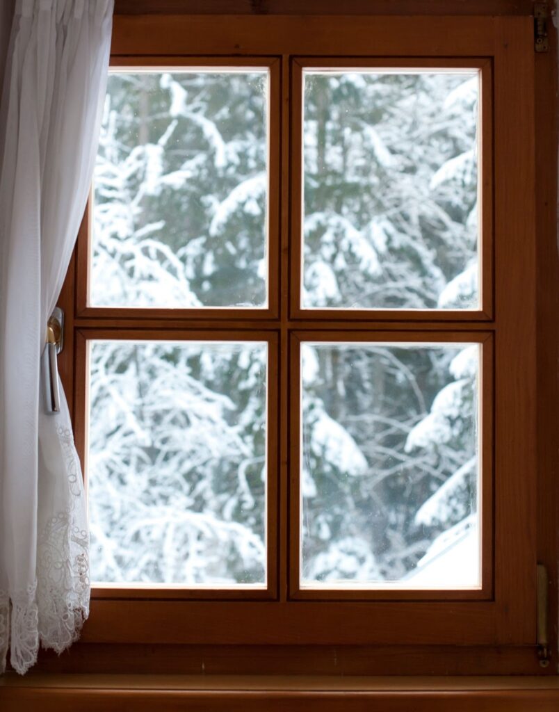 A double-pane window adorned with a curtain, showcasing a snowy landscape outside.