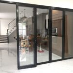 A large glass sliding door beside a staircase, featuring durable aluminum windows and street car window designs.